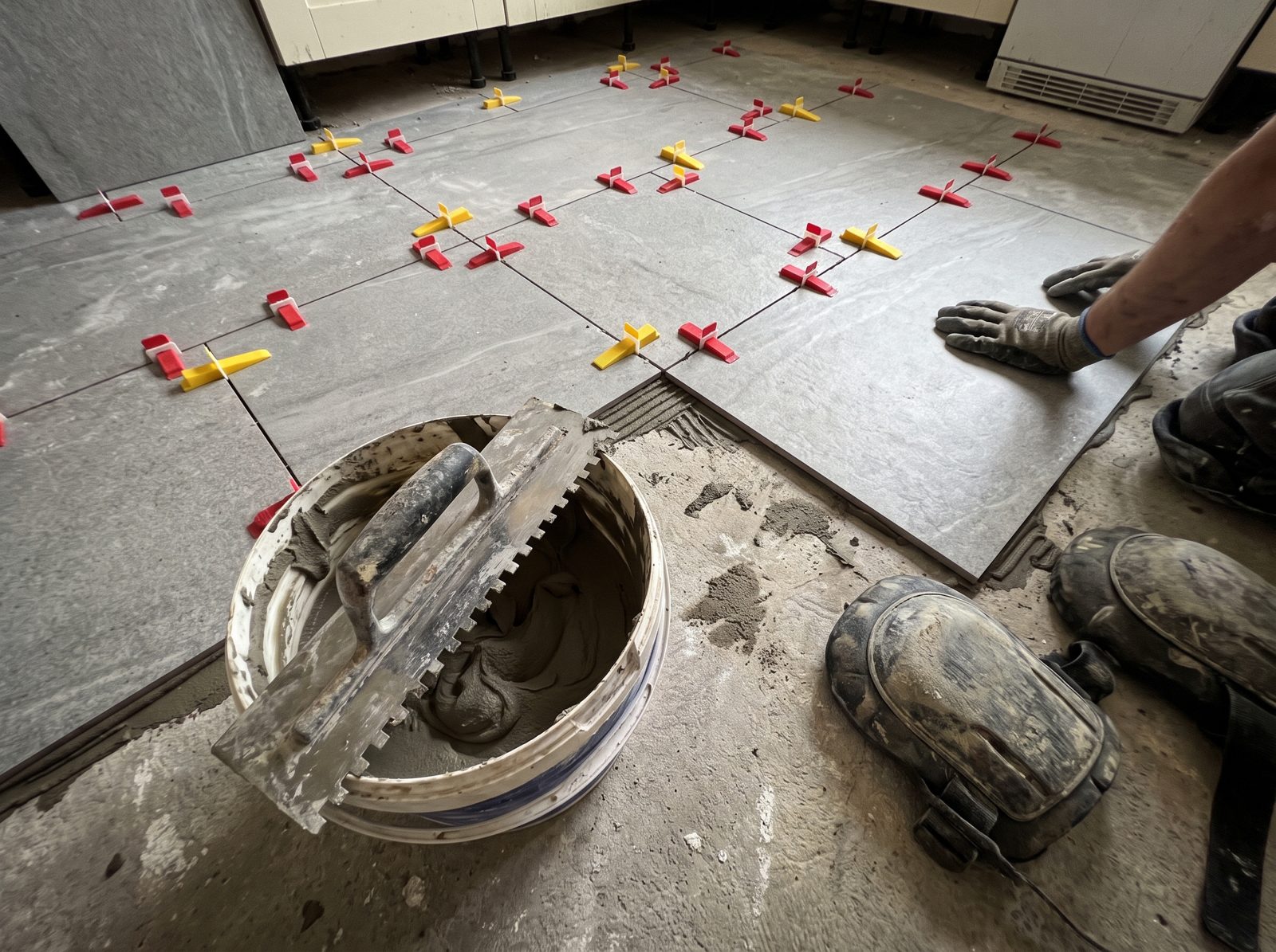 Large grey floor tiles being laid with levelling clips and a notched trowel